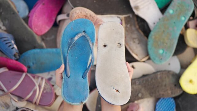 Hands holding two worn-out flip-flops, discarded footwear and shoe waste contribute to global pollution