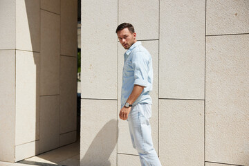 Young man in casual attire standing outside modern building, looking back with a curious expression