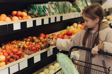 Cheerful teen girl shopping for organic fruits without plastic bags in local food store. Vegan zero waste girl choosing fresh fruits and vegetables in supermarket. Part of a series