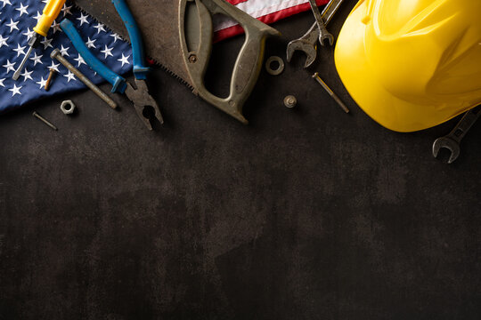Labor Day concept featuring construction tools and yellow hard hat on dark background with American flag