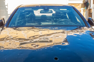 Significant hail damage to a parked vehicle. The windshield is extensively cracked, and the hood is...