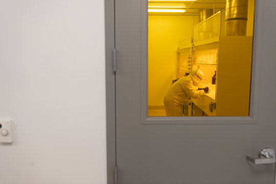 Scientist working in yellow light clean room full PPE bunny suit