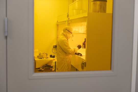 Scientist working in yellow light clean room in full PPE bunny suit