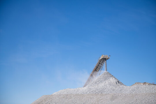 Industrial conveyor belt dumping rock debris at  mine with brigh