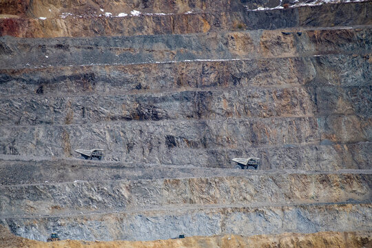 Two heavy-duty industrial dump trucks decend into an open pit mi