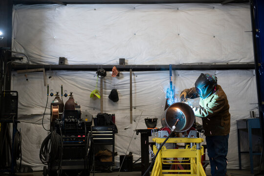 Welder working on a section of industrial pipe in his repair wor