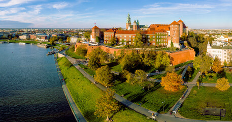 Krakow, Poland. Royal Wawel castle and cathedral, Vistula river, boulevards, promenades and autumn trees with golden leaves. Walking people, harbor and boats. Aerial panorama in sunset light