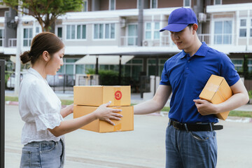 A cheerful Asian woman receives a package from a delivery man in uniform at her doorstep. The courier hands her a paper bag as she signs a receipt using her mobile, completing the home delivery servic