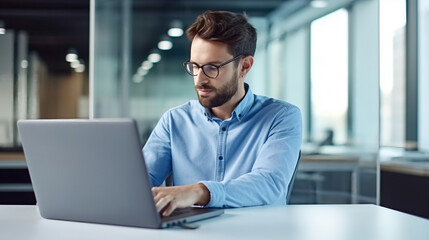 portrait of a businessman working on a laptop in a modern office, wearing a blue shirt and glasses. 