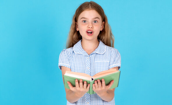 Surprised young girl reading a book aloud, wearing a school uniform, standing against a blue background. Concept of learning and expression