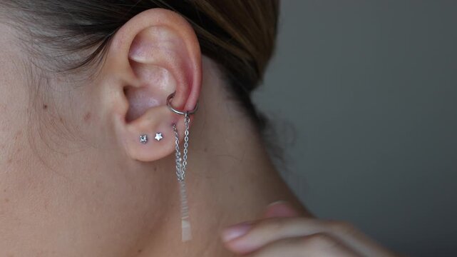 Ear piercing. Young woman wearing three different silver earrings on her ear. Jewelry with gemstones, accessories. Creative earrings