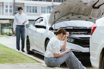 A young Caucasian man and an Asian woman inspect a damaged car after an auto accident. The insurance agent examines the vehicle, writing a report while gathering evidence for the claim investigation a