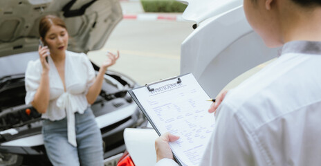 A young Caucasian man and an Asian woman inspect a damaged car after an auto accident. The...