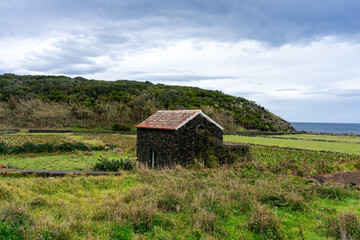 Obraz premium Rustic stone house built with volcanic rock, set against the backdrop of the Atlantic Ocean on Terceira Island, Azores, Portugal. Perfect blend of natural beauty and traditional architecture.