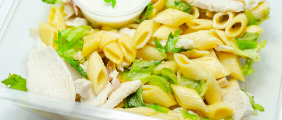 A box of takeaway with pasta, a white sauce and green vegetables