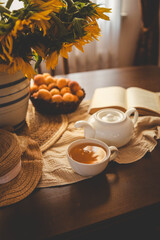 Cup of tea, open book and sunflowers in a vase, summer mood
