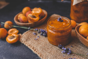 Homemade apricot jam with lavender flowers, surrounded by fresh apricots and lavender sprigs on a rustic burlap cloth