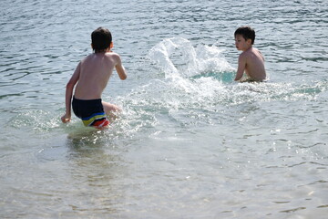 Happy children, aged 10-12, swimming and splashing in lake, river or sea, beach activity