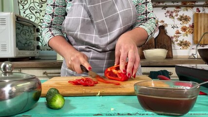 Culinary concept, preparation ingredients for homemade food. A young adult woman in an apron cooking a meal, cutting vegetable on a kitchen counter indoors. Home cooking and gastronomy passion