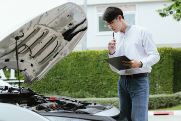 A male mechanic inspects a broken-down car on the roadside, while a female insurance agent provides assistance. The Caucasian driver, holding a clipboard, discusses the damage and files a claim for re - Powered by Adobe