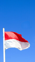 The red and white Indonesia national flag is waving againts clear bright blue sky. free space for text.