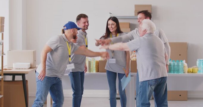 A group of happy people in uniform raise their hands, a gesture of teamwork. Meeting of volunteers at a food warehouse, slowmotion. Altruism concept, free help to those in need - Powered by Adobe