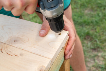 screwing a plank of wood to a wooden frame with a screw gun to make a simple table