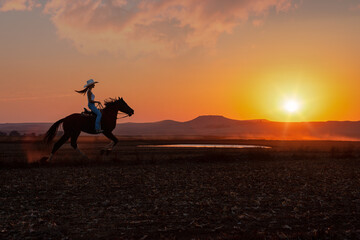 silhouette cowgirl in the sunset riding galloping in the prairie near a waterhole