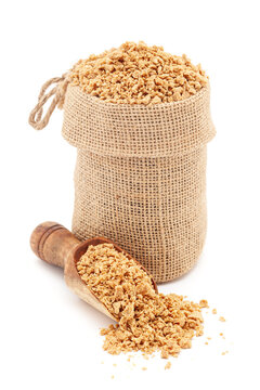 Close-up of Organic Soya Granules (Glycine max), in a jute bag and on a scoop, Isolated on a white background.