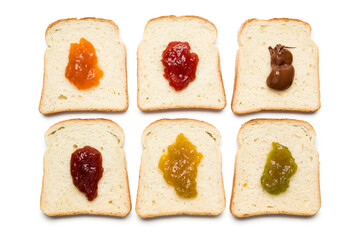 Slices of white bread with variety of jam on white background, top view.