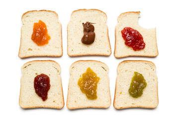 Slices of white bread with variety of jam and bitten on white background, top view.