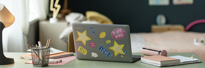 Header background image of open laptop decorated with stickers on desk in childs room with school...