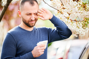 Man allergic suffering from seasonal allergy at spring in blossoming garden at springtime. Man...