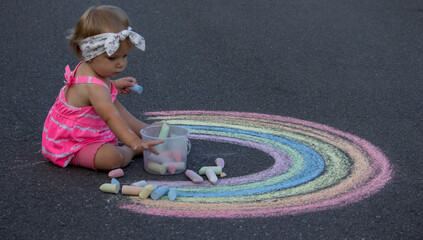 Fototapeta premium a little girl draws a rainbow on the asphalt with chalk. Selective focus