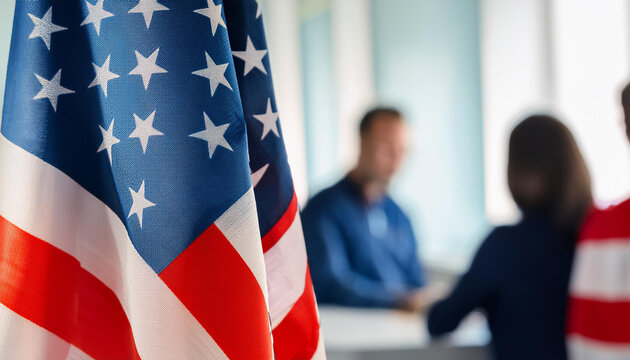 Close-up of American Flag with Out-of-Focus Business Professional Giving a Speech in the Background, Symbolizing Patriotism and Leadership in Corporate or Governmental Settings