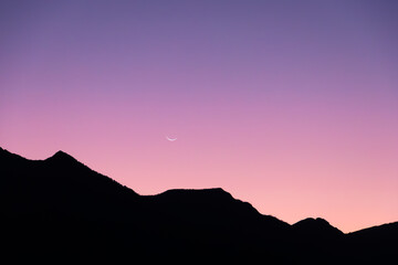 silhouette of mountains in colorful sunset and moon in the sky