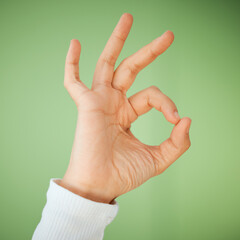 Okay, person hand and sign with like, yes and emoji gesture in studio with agreement and thanks. Approval, success and positive review with closeup and social media symbol with green background