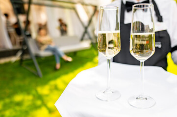 Two champagne glasses on a table at an outdoor event, with blurred guests in the background, creating a festive and elegant atmosphere. Perfect for celebrations, weddings, or social gatherings.