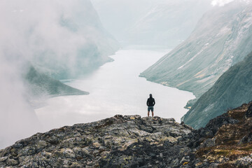 hiker on the top of mountain looking out over fjord mist lifting