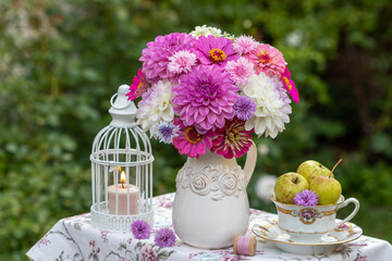 Tisch-Arrangement mit Blumenstrauß mit lila und weißen Dahlien, Zinnien und Nelken, Äpfeln in...
