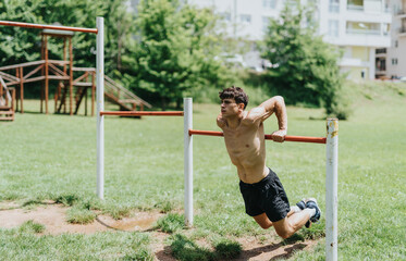 Fit man exercising outdoors on horizontal bars in a park, demonstrating strength and fitness.