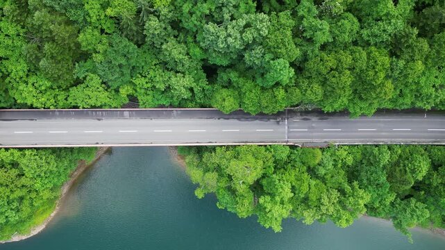 Hokkaido, Japan: Aerial overhead drone footage of a car on the road along the Chubetsu reservoir and the Ishikari river at the foot of the Asahidake mountain in Hokkaido in summer in Japan