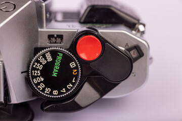 A close-up shot of an antique camera with its red shutter button visible. The camera is positioned against a white background.