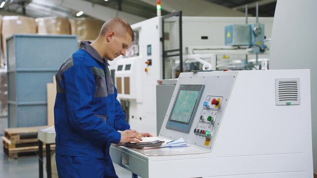 Working day. Employee, worker of corrugated cardboard factory stands near control panel of production equipment. Male process engineer, skilled worker analyzes CNC indicators of production equipment.