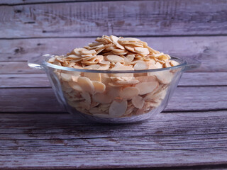 Glass bowl holding thinly sliced golden-brown almonds on a rustic wooden table, perfect for use in salads, desserts, or as a nutritious snack.