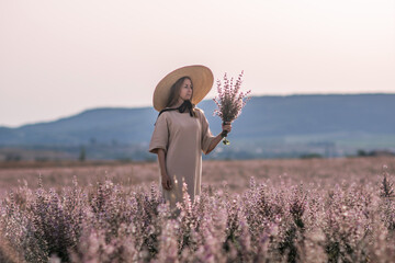 Woman Flowers Field - A woman wearing a hat and dress stands in a field of pink flowers with mountains in the background.