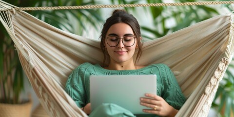 young woman relaxing in a hammock, working on a laptop computer, enjoying the outdoors and nature, green sweater, casual clothing.