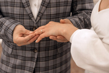 Obraz premium Groom in a wedding suit puts a ring on the finger of a bride in beautiful white dress. An exciting moment of the wedding ceremony