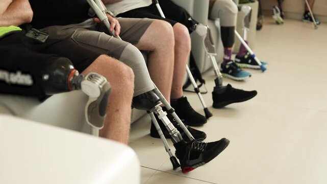 Diverse group of amputees sit together with prosthetic legs and crutches.