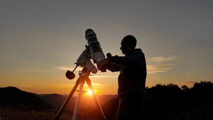 Amateur astronomer looking at the evening skies, observing planets, stars, Moon and other celestial objects with a telescope just before sun down.